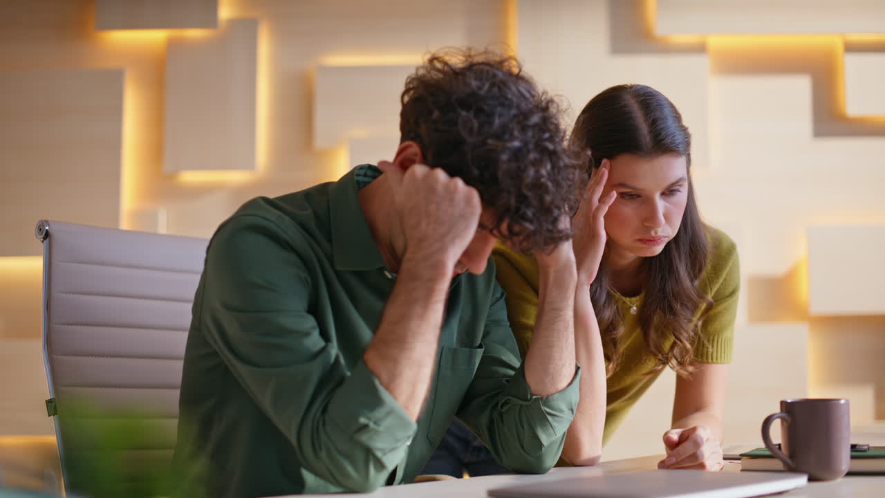 Two colleagues working together on a laptop, facing problems and stress at the office