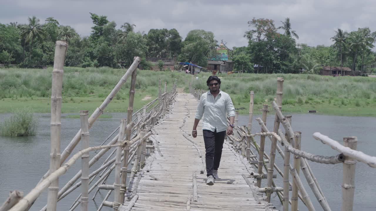 A man stands on the bamboo bridge built over the Damodar River and enjoys the natural beauty.