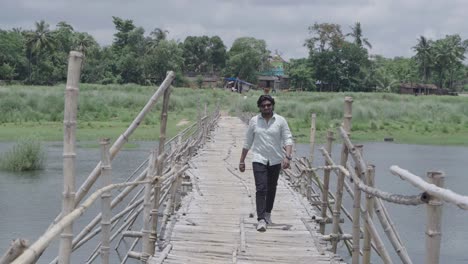 a man stands on the bamboo bridge built over the damodar river and enjoys the natural beauty.