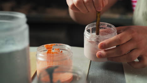 the person is stirring a pink glaze in a jar, preparing it for pottery decoration - close up