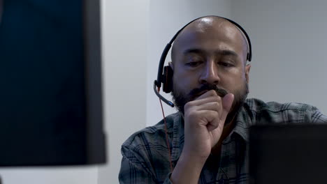 an indian call centre employee seated at his office desk with his clutch fist covering his face, the man troubled and in deep thought on how best to approach his manager with a personal issue