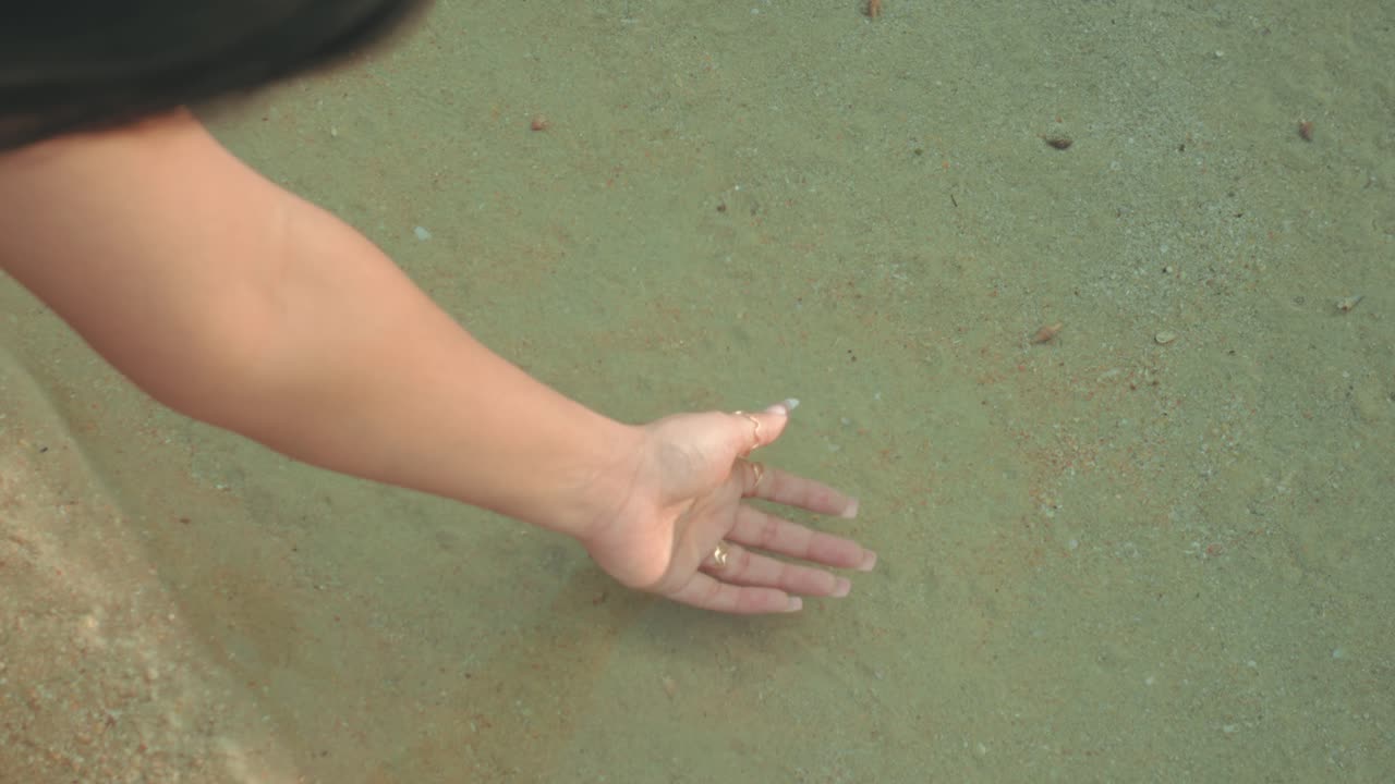 Hand touching water on sandy beach, serene moment, calming vibe