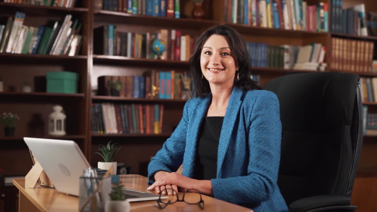 una mujer de mediana edad se sienta en una mesa con una computadora portátil frente a ella