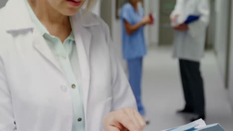 Female-surgeon-checking-medical-reports-while-colleague-discussing-in-background