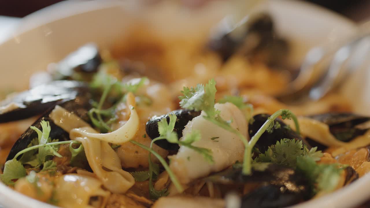Macro view of a hot seafood chowder bowl with fish, squid, mussels, scallops, and fresh herbs, under warm, natural lighting with shallow depth of field