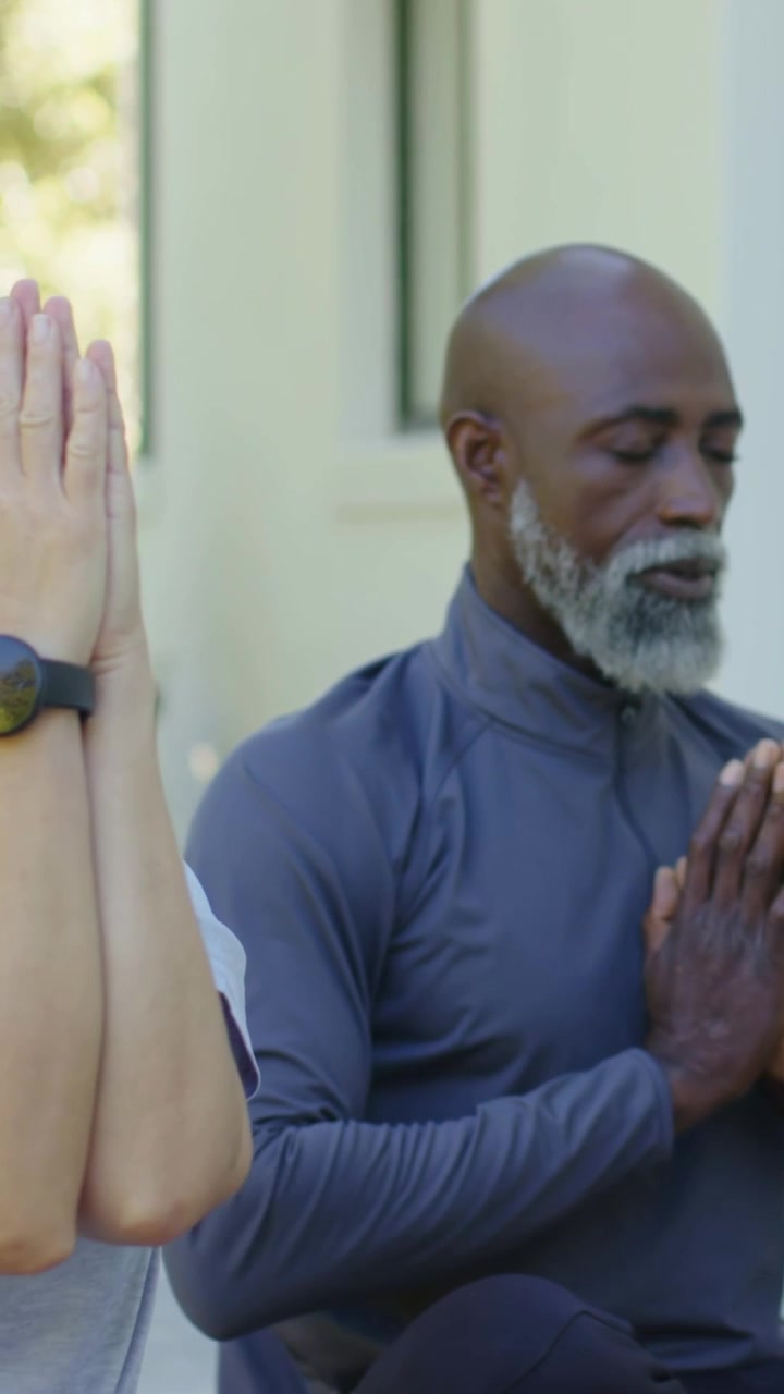 Lodret video: Kvinde i træningstøj starter yoga på terrassen, sænker sig ned i bønne-stilling med samlede håndflader.