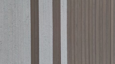 revealing alternating strips of light-bleached and dark-turned soil furrows carved into a vast agricultural field, creating a minimalist pattern under soft daylight, overhead in slow motion