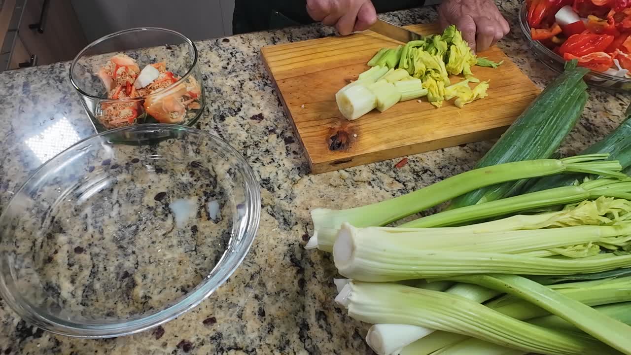 Sedano verde fresco tagliato a fette con un coltello su un tagliere di legno al chiuso