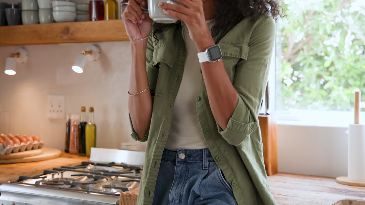 Woman enjoying coffee in modern kitchen, wearing smartwatch and casual outfit, at home