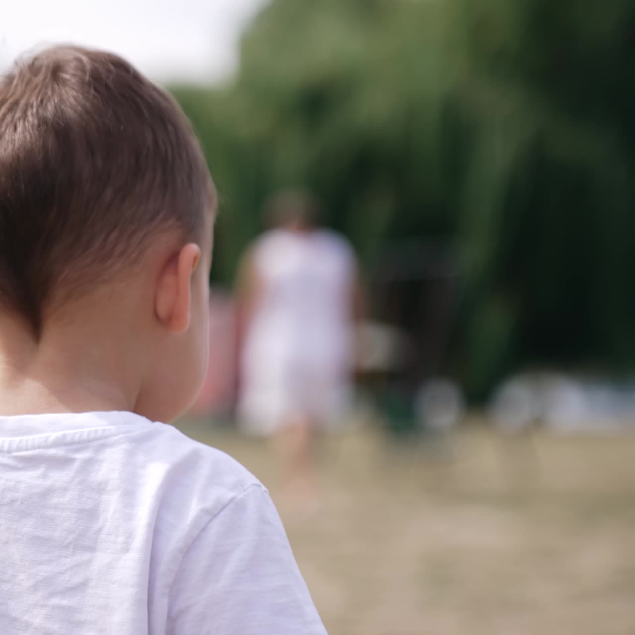 Adorable Caucasian kid bending head left and right. Portrait of a toddler outside in summer. Blurred backdrop