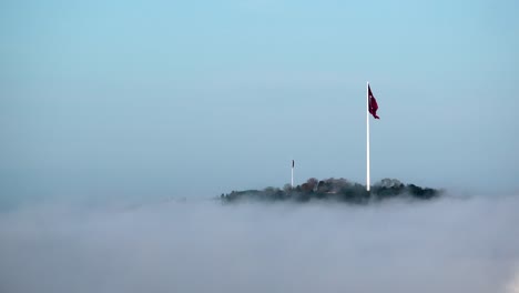 turkish flag atop a hill, shrouded in morning fog