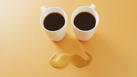 video de dos tazas de café negro y bigote falso rubio en fondo amarillo con espacio para copiar.