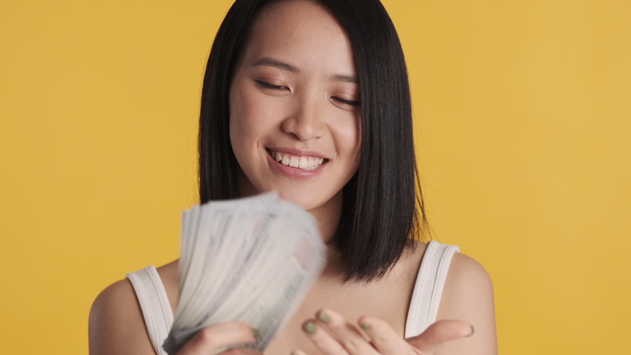 Asian woman looking happy while holding money on camera.