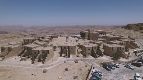 Aerial-view-over-a-beautiful-architecture-stone-built-hotel-on-a-crater-cliff-desert-landscape,-crossing-the-accommodations-and-over-the-pool-1