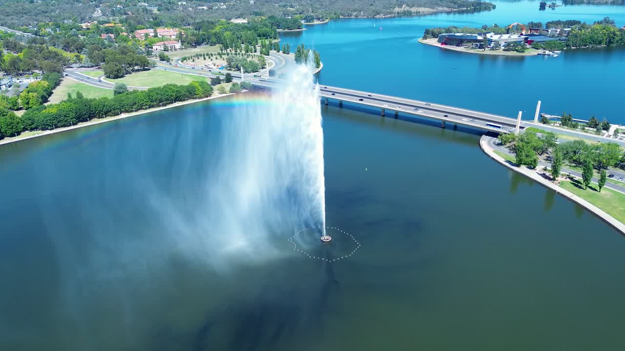 Drone aerial landscape of rainbow in water spraying fountain jets in Lake Burley Griffin with cars on road bridge river overpass Canberra city ACT Australia landmark travel tourism infrastructure