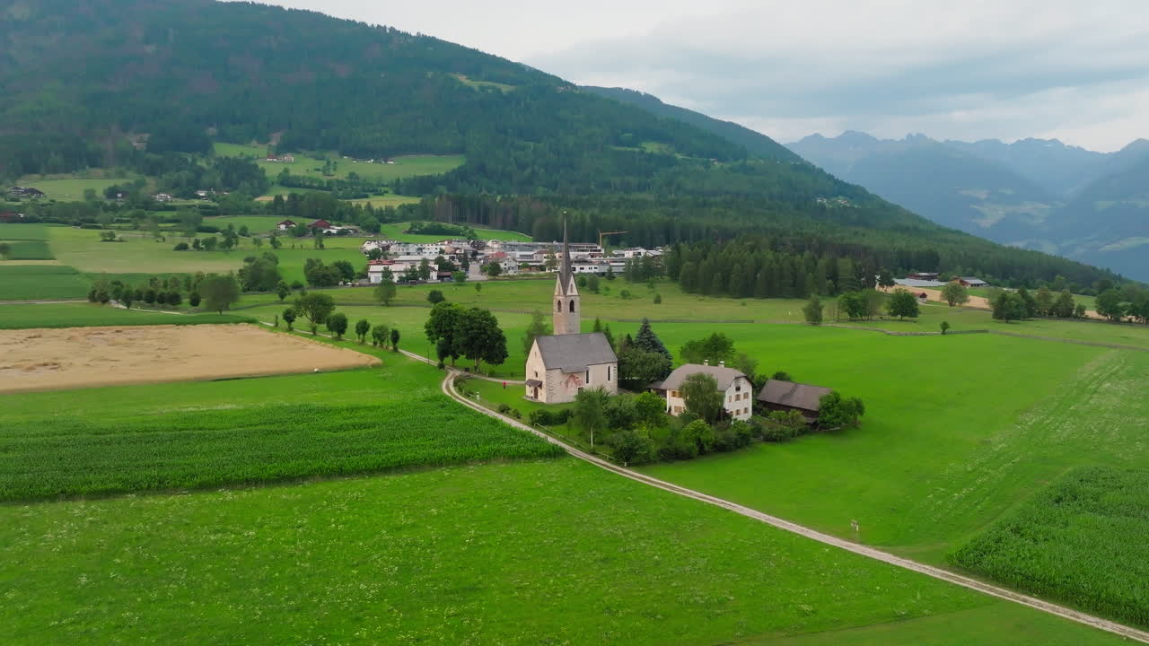 Drone slowly moves over St. Valentin church and lush farmland near Pfalzen, Dolomites