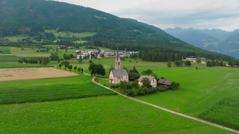 drone slowly moves over st. valentin church and lush farmland near pfalzen, dolomites