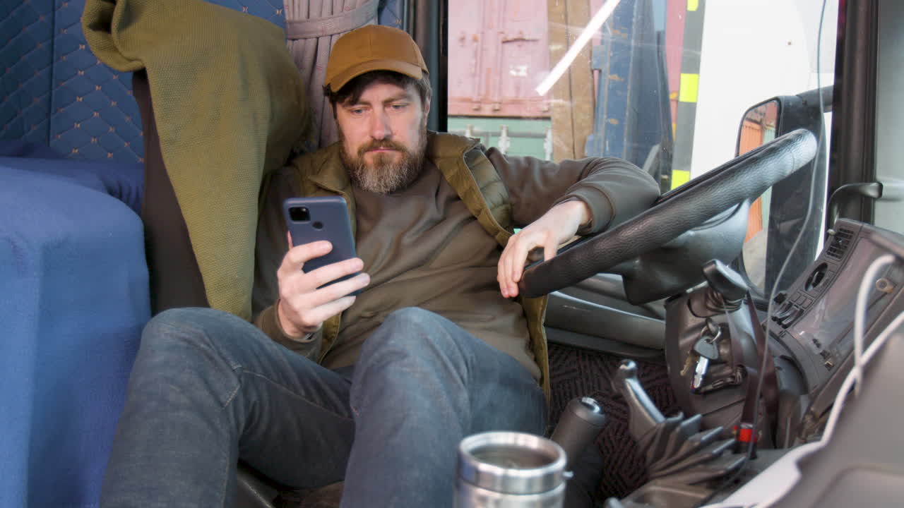 Trabajador con gorra y chaleco tumbado en el asiento del camión mientras usa el smartphone
