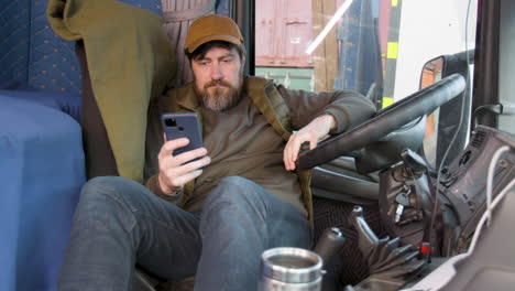 worker wearing cap and vest tumbado lying on truck seat while using smartphone