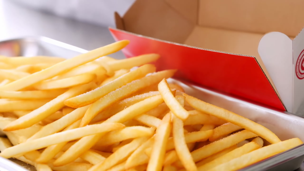 Overflowing Golden Fries From Red Box Pouring Onto Metal Tray, Crisp Salted Sticks Tumbling From Cardboard