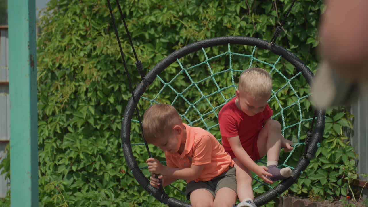 Caucasian Boys Laughing Together On Swing In Backyard, Heads Leaning As They Giggle In Warm Sunlight, Leafy Hedge And Fence Framing Candid Playful Summer Scene, Lively CloseUps Of Carefree