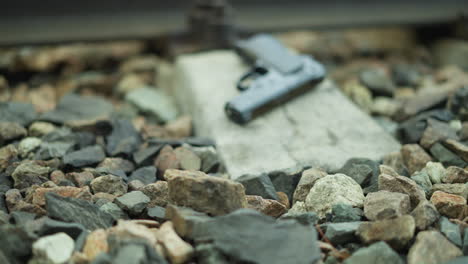 a close view of a handgun lying on the rocks of a railway track, with the blurred background of the rail and bolts, the focus is on the gun and the rocky ground