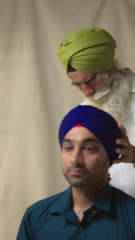 a sikh man wearing a turban, helping another man put on his turban.