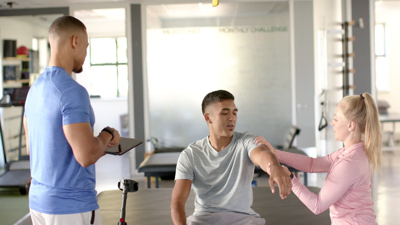 Physical therapist assisting man with arm exercises, another therapist taking notes