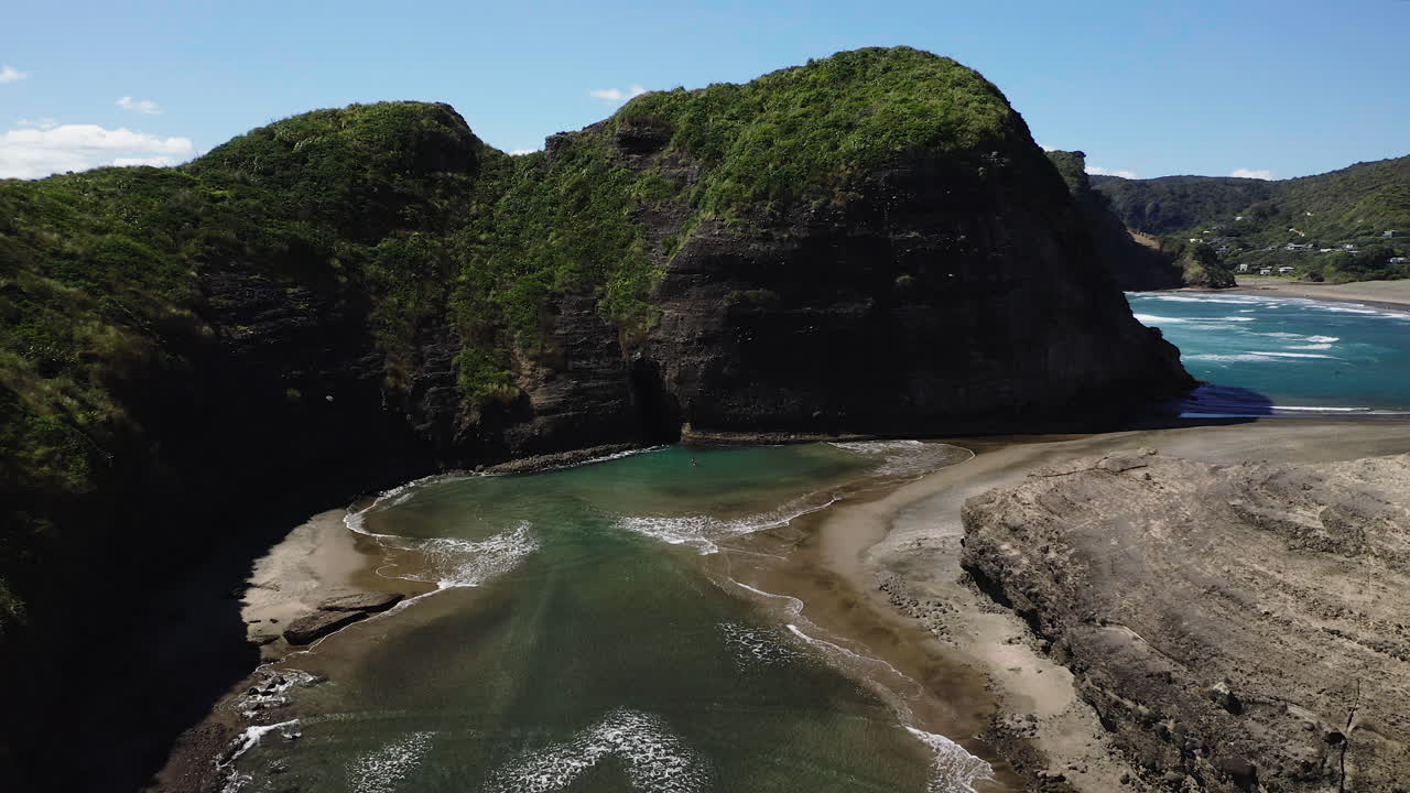 Aallot kulkevat kapeaa uomaa pitkin muodostaen matalia lammikoita kultaisella ja mustalla hiekalla, Piha Beach Uusi-Seelanti