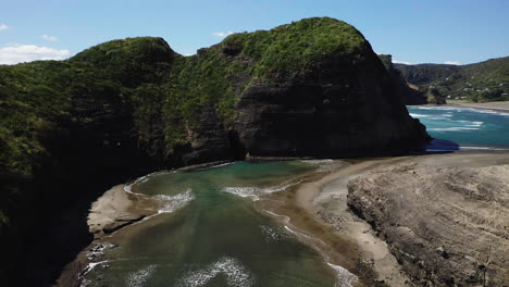 Waves-travel-up-narrow-inlet-creating-shallow-pools-on-the-golden-and-black-sands,-Piha-Beach-New-Zealand