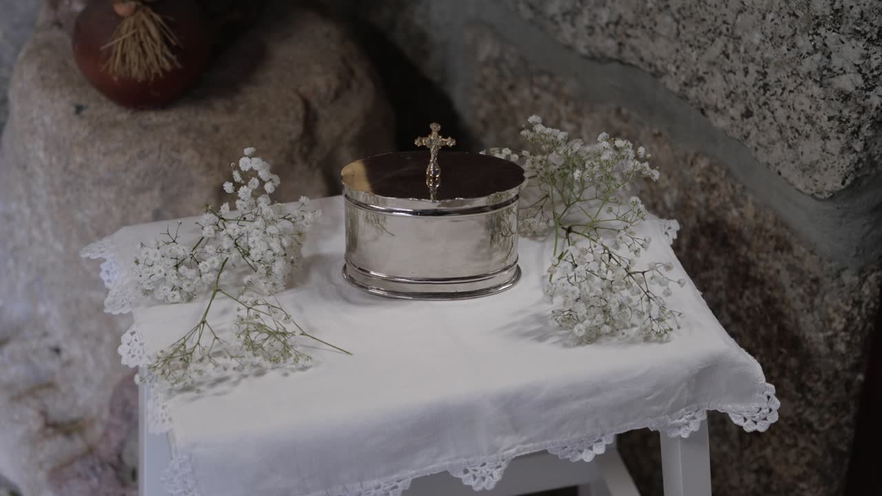 Silver vessel with cross and white flowers on lace altar table by stone wall