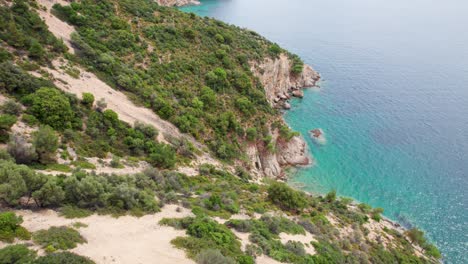 Vista-De-Arriba-Hacia-Abajo-Sobre-Una-Costa-Rocosa,-Agua-Turquesa,-Vegetación-Exuberante,-Playa-Fari,-Isla-De-Thassos,-Grecia