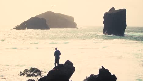 silueta de un hombre de pie en una roca con los brazos abiertos contra la playa de monsteiros en sao miguel, isla de las azores