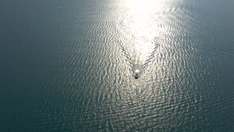 Toma-Aérea-Estática-De-Un-Pequeño-Yate-Navegando-Lentamente-Por-Las-Tranquilas-Aguas-Del-Lago-De-Garda