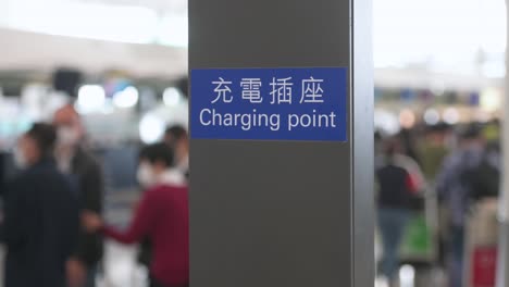 a sign indicates the location of a battery charging station, a free airport facility, for passengers to use and charge their electronic devices at the airport terminal hall in hong kong