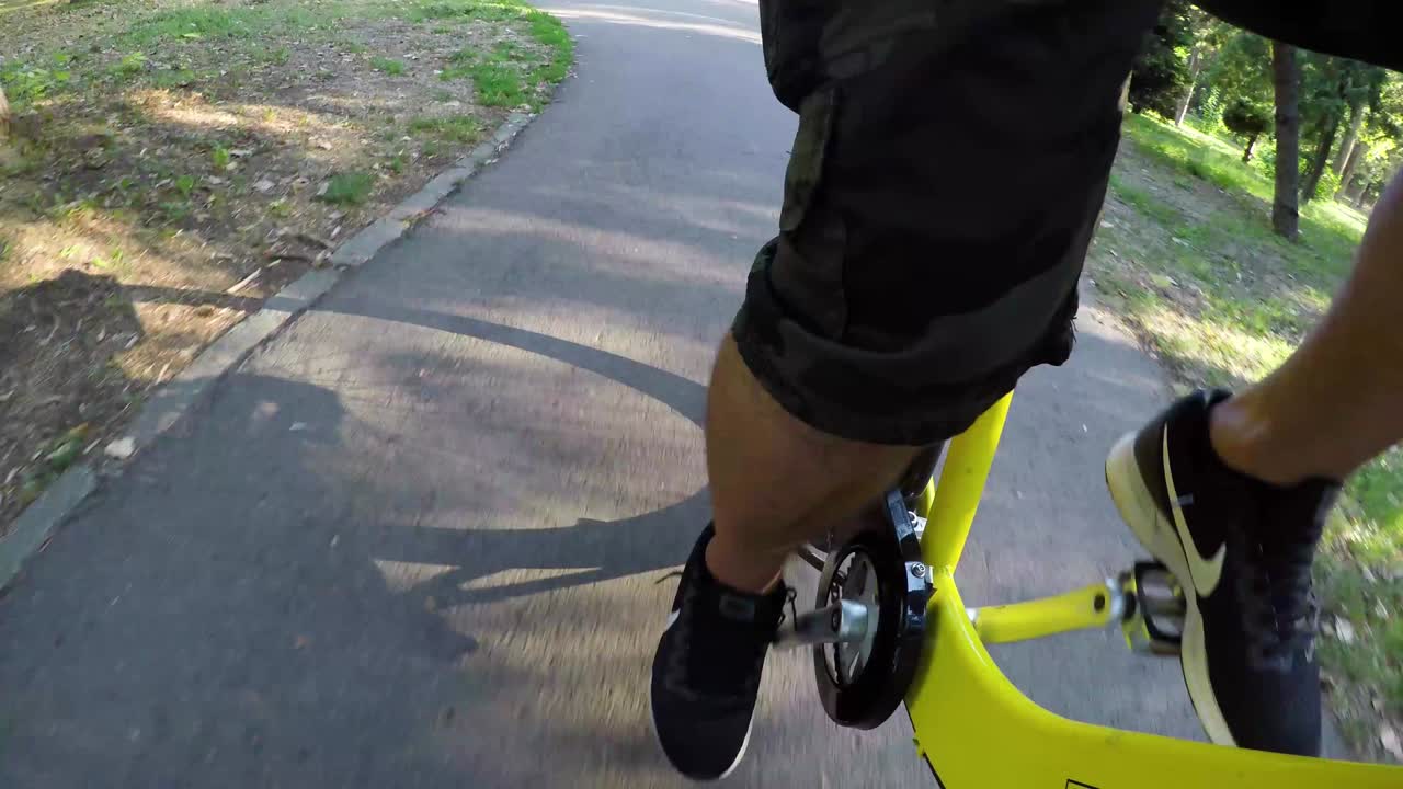 Cyclist's feet pedaling on a yellow bicycle in a sunny day in park.