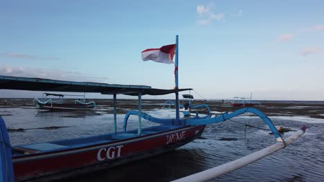 Bandera-De-Indonesia-Ondea-En-El-Viento-En-El-Paisaje-De-La-Playa-De-Sanur,-Mar-Y-Horizonte,-Símbolo-Nacional,-Bali,-Denpasar