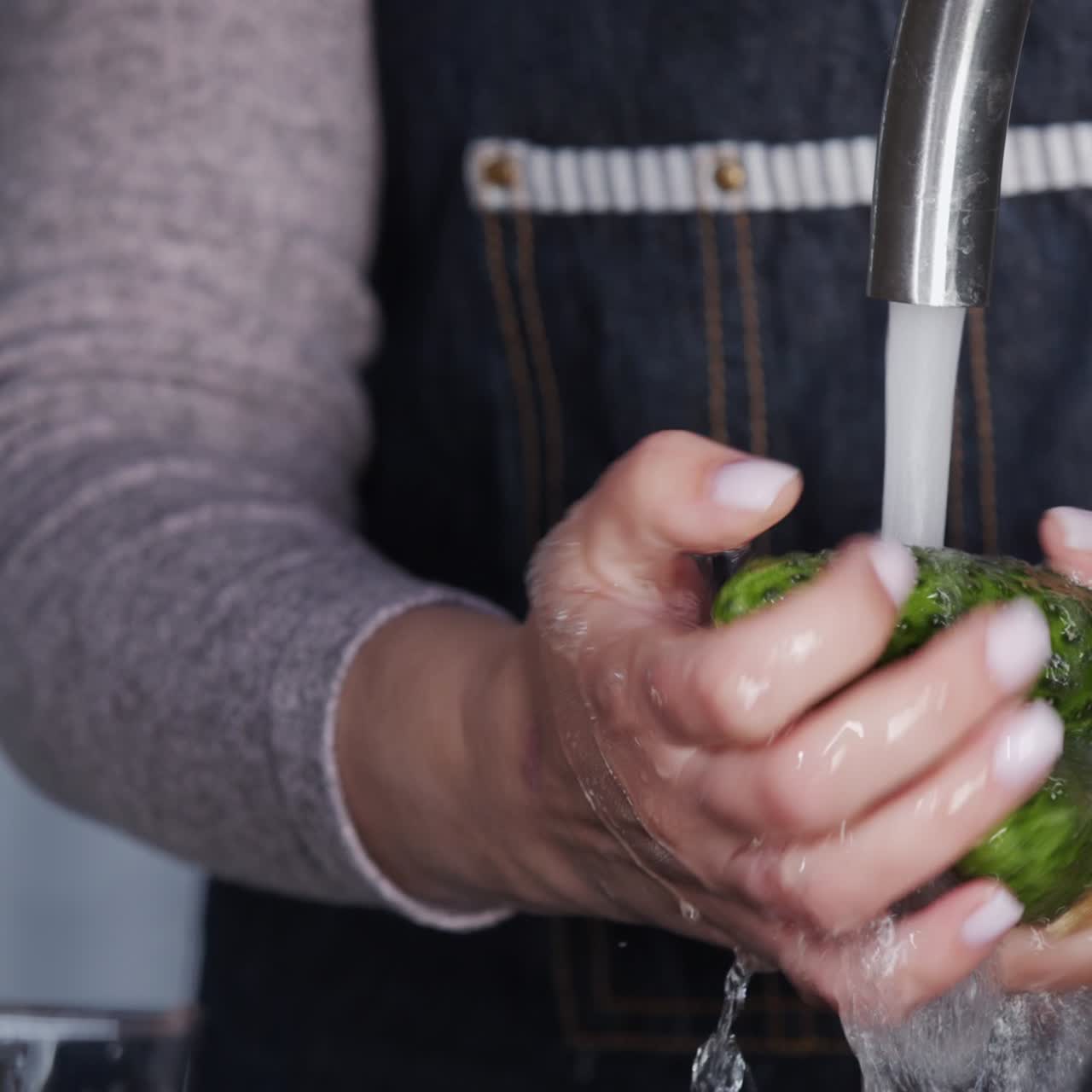 uma mulher lava pepinos sob uma corrente de água de uma torneira