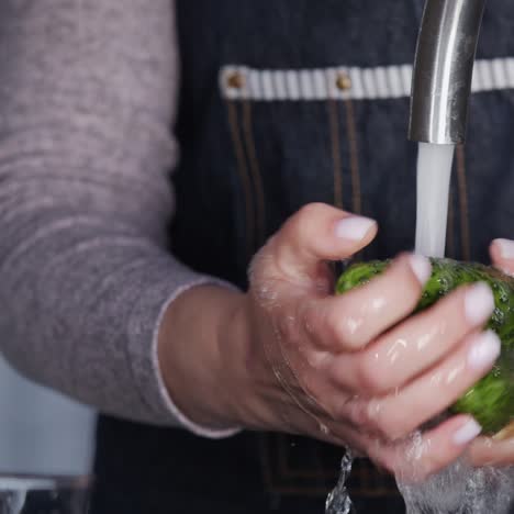 una mujer lava pepinos bajo un chorro de agua de un grifo