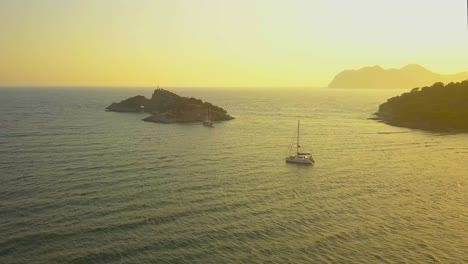 a drone flies awayfrom  a small island off fethiye.  a catamaran sails peacefully along