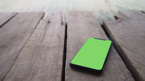 smart phone place on wood background, green screen telephone, close up display mobile phone with mock up, chroma key monitor, close-up call phone on old wooden board, slow motion handheld top view.