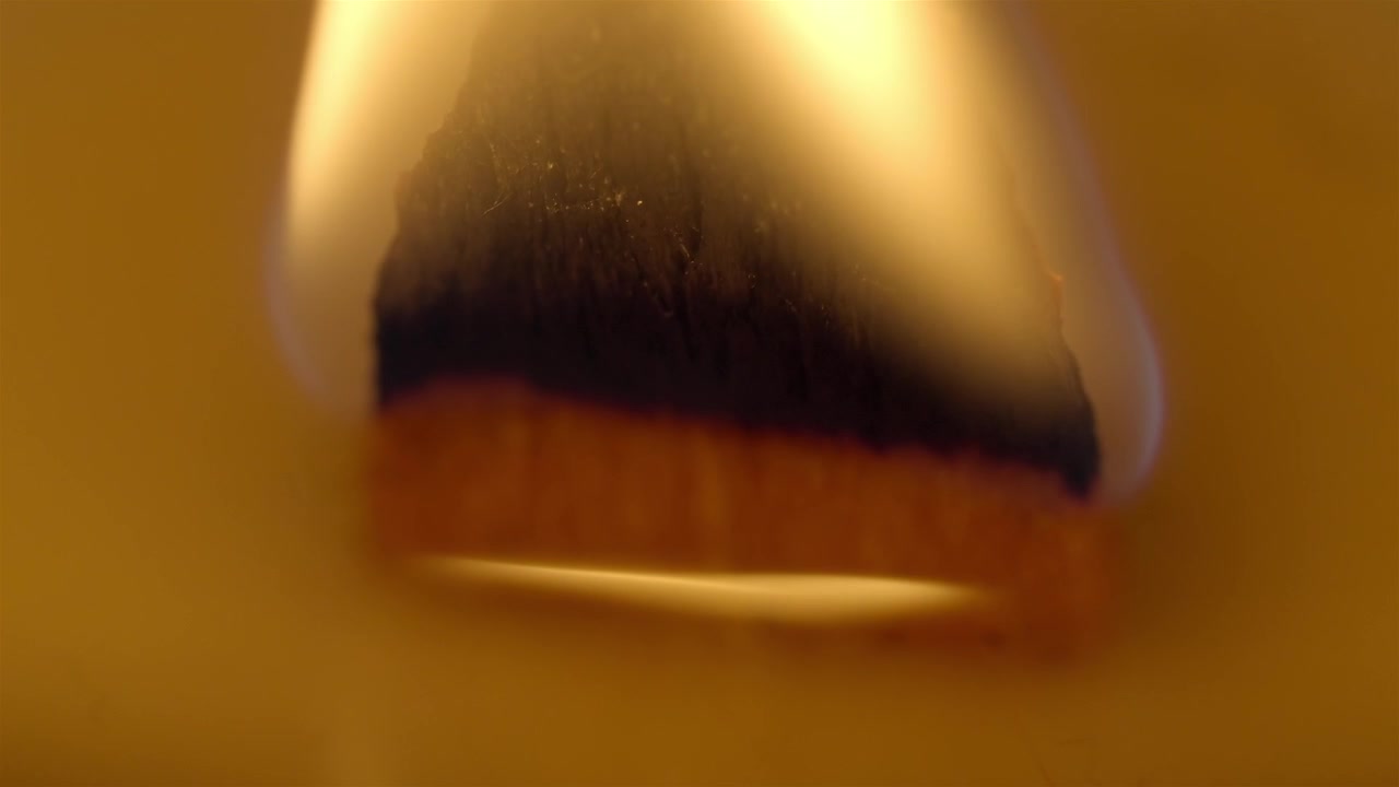 Warm candle flame light glows over the wick and melted wax in extreme macro.