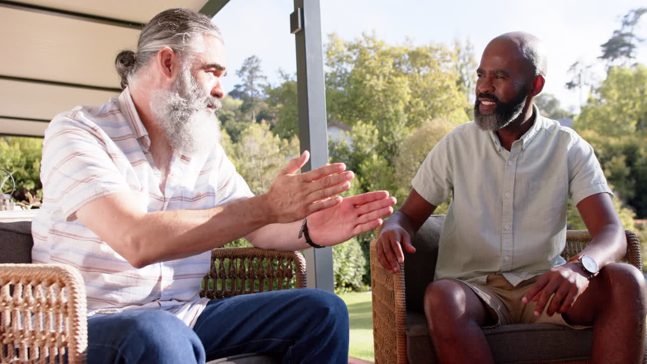 Amigos mayores conversando y gesticulando mientras están sentados en sillas de patio al aire libre