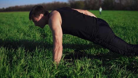 the young guy assiduously does push-ups on one hand. complicated. beautiful nature, meadow, clear sky. overview footage