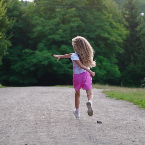 back view of a girl running in the park. happy little girl with long hair having fun alone on the natural green background in summer.