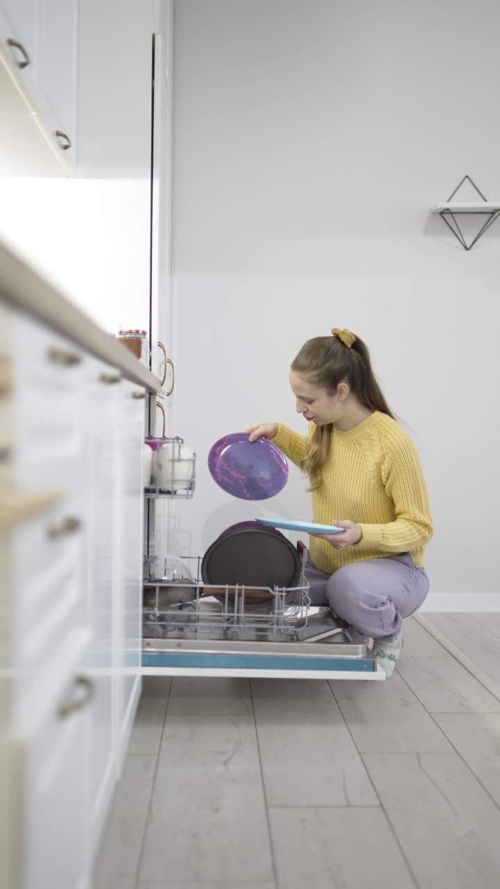 Video vertical que muestra a una mujer colocando platos en un lavavajillas, destacando la organización de la cocina, las tareas del hogar, la limpieza del hogar y el mantenimiento doméstico diario en un entorno interior ordenado.