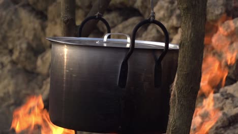 cerca de una olla de cocina de metal colgando sobre un fuego abierto