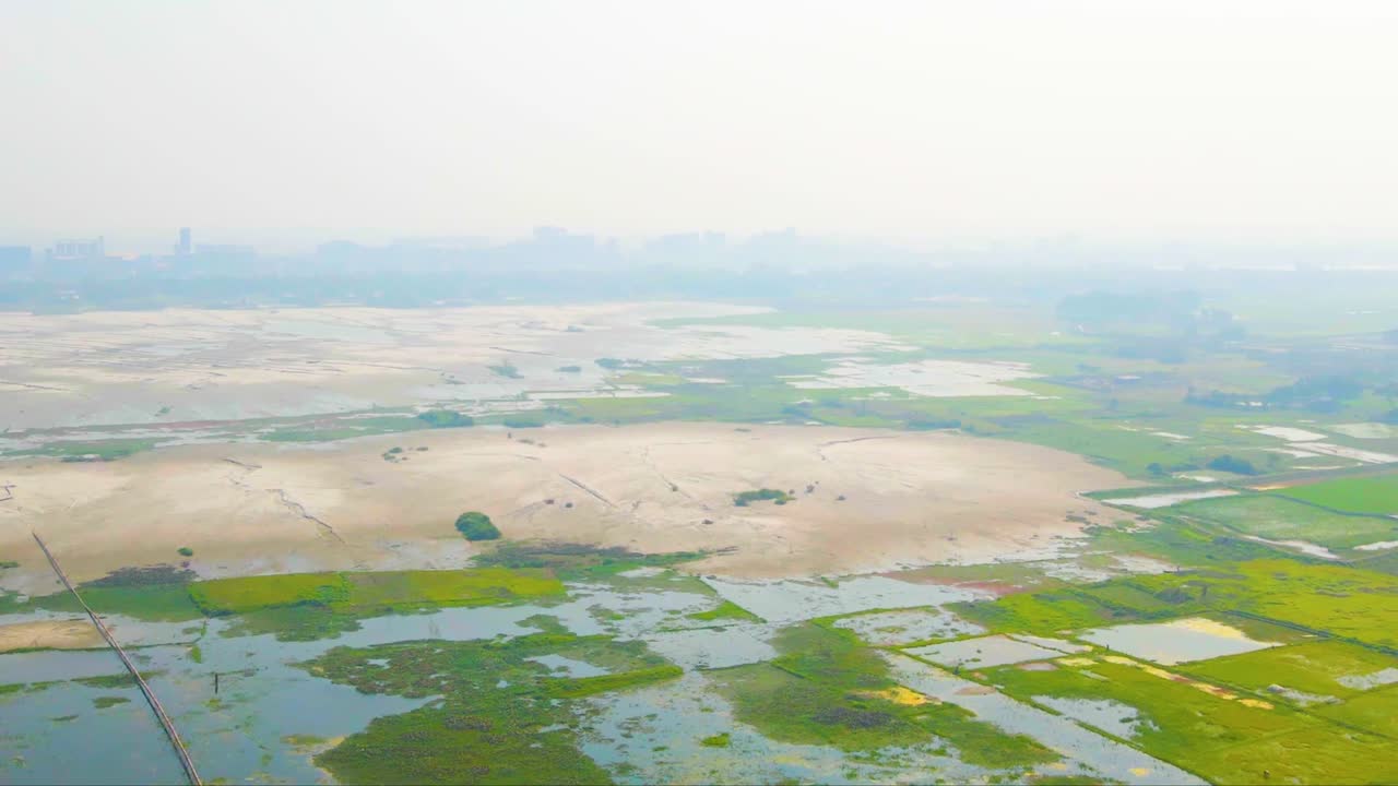 Drone view of Bangladeshi rural wetlands in the countryside of the skyline of a Dhaka City on the horizon.