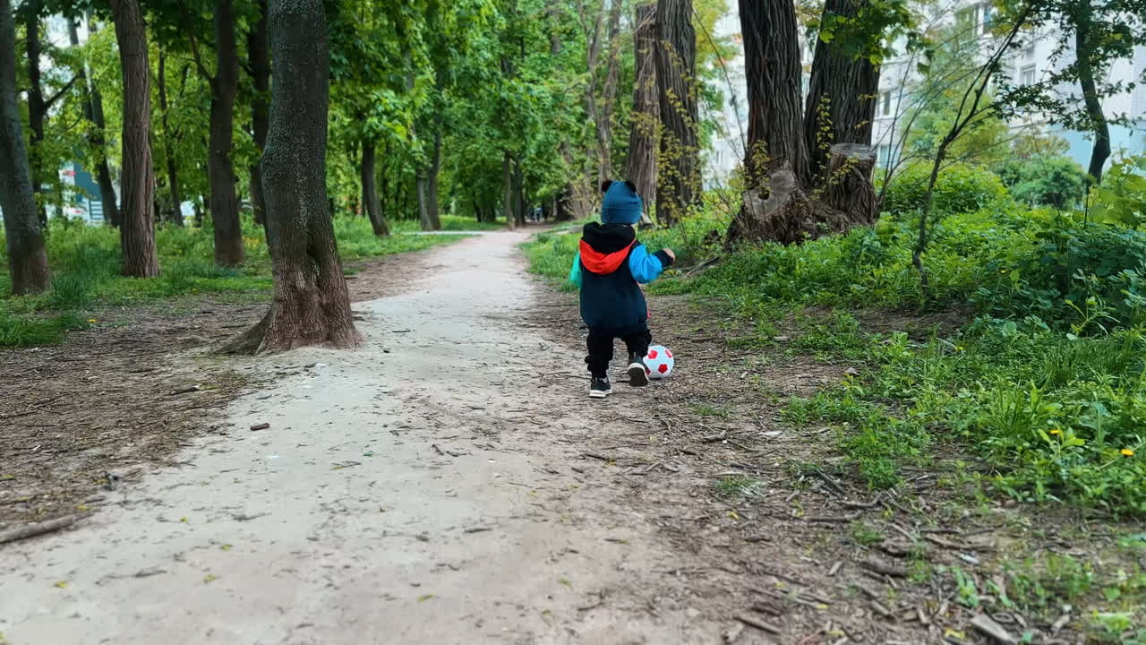 Following the little boy running quickly by the ball. Baby grabs the ball happily and turns back.