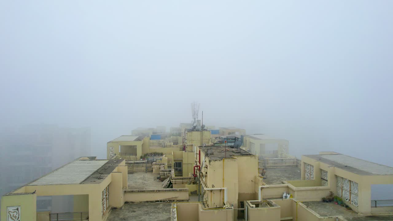 Ripresa aerea con drone che vola basso sopra un edificio giallo circondato da una fitta nebbia, che mostra gli inverni a Delhi, Jaipur, Chandigarh, stazioni collinari dell'India